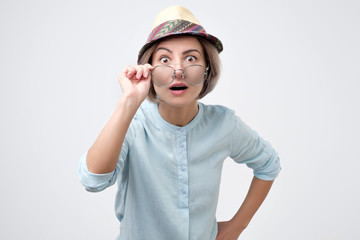 Surprised young woman in hat and glasses with open mouth can not believe her eyes.
