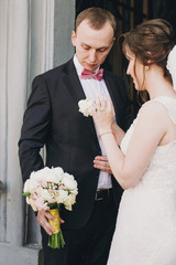 Happy Bride putting on stylish boutonniere on groom suit at doors after wedding ceremony in church....