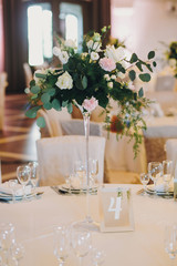 Stylish decorated tables with roses bouquets, plates,glasses, cutlery at wedding reception. Luxury catering. Christmas and New Year feast. Celebrations and party concept.