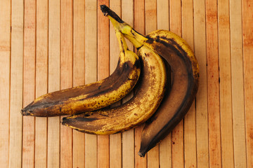 3 rotten and spoiled brown bananas on wooden background