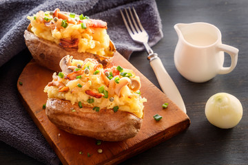 Baked potatoes with bacon and mushrooms in a rustic way on a wooden board. Close-up.