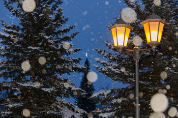 Новогодняя композиция из уличных фонарей на фоне заснеженных елей и снегопада. 