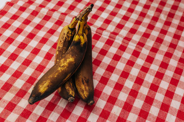 3 rotten and spoiled brown bananas on red checkered background