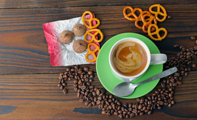 A cup of coffee on a wooden table, grains of coffee, chocolate and cookies.