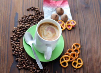 A cup of coffee on a wooden table, grains of coffee, chocolate and cookies.