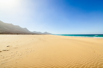 Fototapeta na wymiar Fuerteventura, Canary Islands, Spain. Cofete beach with endless horizon and traces on sand. Volcanic hills in the background and Atlantic Ocean.