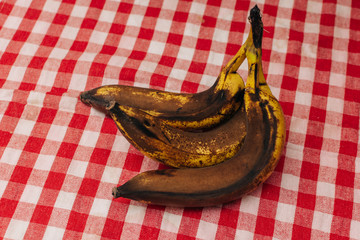 3 rotten and spoiled brown bananas on red checkered background