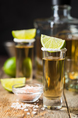 Mexican Gold Tequila shots with lime and salt on wooden table over black background