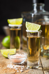 Mexican Gold Tequila shots with lime and salt on wooden table over black background
