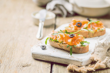 Healthy breakfast salmon sandwich with cream cheese and arugula on wooden background