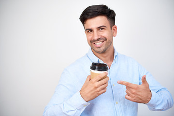 Portrait of happy young man standing with disposable cup of coffee and pointing at it isolated on white background