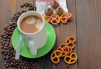 A cup of coffee on a wooden table, grains of coffee, chocolate and cookies.