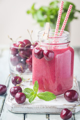 Healthy cherry smoothie with frozen strawberry, coconat water and honey in glass on white wooden table.