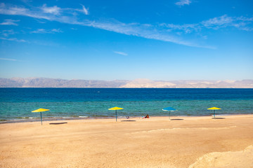 Beach on the shore of the Red Sea. Umbrellas, water and beach. Resort in the Aqaba, Jordan next to Israel Ejlat.