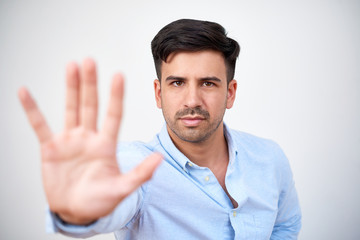 Picture of serious young stubble man dressed in blue shirt posing isolated over white background while make stop gesture