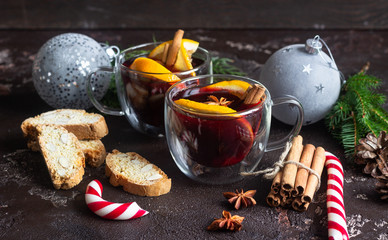 Glass cups of hot mulled wine or gluhwein with spices and orange pieces on dark brown background....