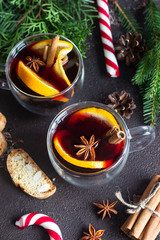 Glass cups of hot mulled wine or gluhwein with spices and orange pieces on dark brown background. Christmas mulled wine. Traditional drink on winter holiday. Copy space.