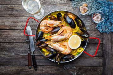 Traditional spanish seafood paella in a fry pan on a wooden old table, top view