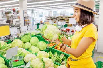 Happy asian Woman shopping for vegetables and looking at cauliflower cabbage in supermarket, healthy food concept