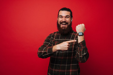 Happy smiling bearded man is poiting at his smartwatch