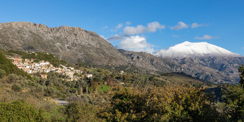 Fototapeta na wymiar Traditional village in mountain with snowy mountains and blue sky in background. Crete Greece.
