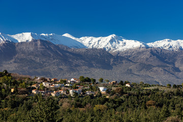 Traditional village in mountain with snowy mountains and blue sky in background. Crete Greece.
