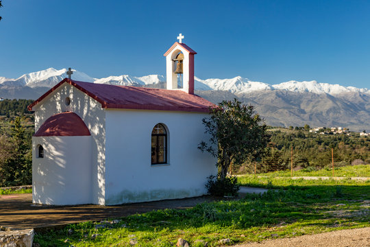 Crete, Greece 12-14-2018. Little Byzantin church with snowy mountains and blue sky in background.