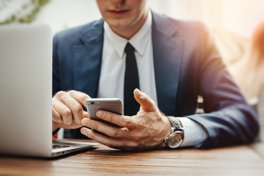 Close up of businessman looking at screen of mobile phone at street cafe.