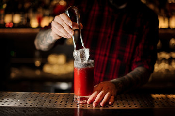 Bartender putting a big ice cube to a glass of a Bloody Mary cocktail