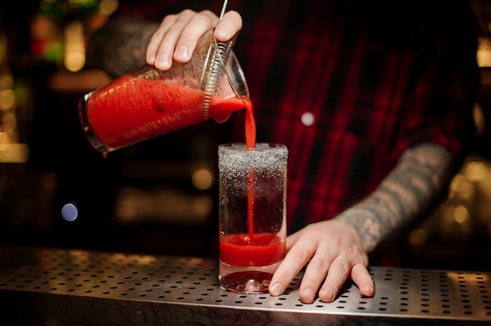 Bartender pouring a Bloody Mary cocktail from the measuring cup
