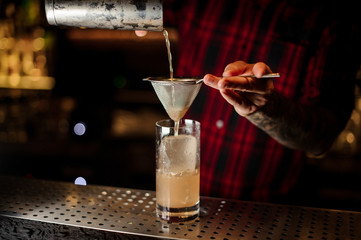 Bartender pouring a Lemonade cocktail from the steel shaker through the strainer