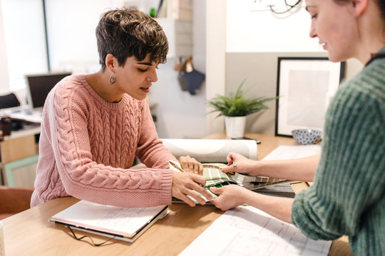 Side view of two women interior designers discussing about blueprints