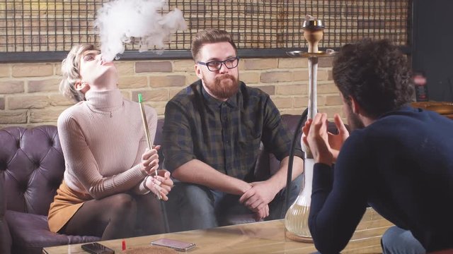 Attractive young men and woman are talking while smoking the hookah. Entertainment and conversation concept