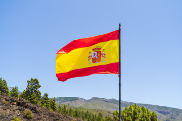 The national flag of Spain against the blue sky and mountains.