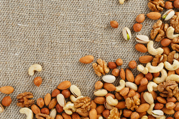 Mix of nuts of cashew, almonds, pistachios, hazelnuts and walnuts is against the background of brown fabric of burlap. Nuts as structure and background, macro
