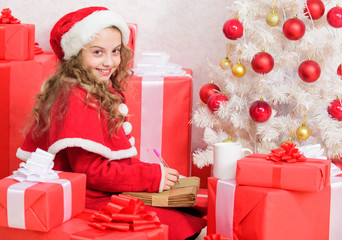 Obraz na płótnie Canvas Wish list. Girl little kid hold pen and paper near christmas tree writing letter. I was good girl all year. Child write letter to santa claus. Child santa costume believe in miracle. Letter for santa