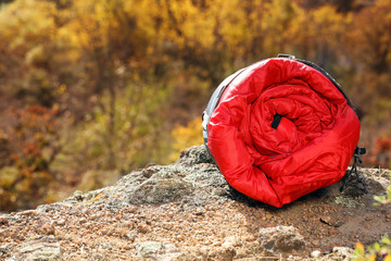 Red sleeping bag on rock outdoors, space for text. Camping equipment