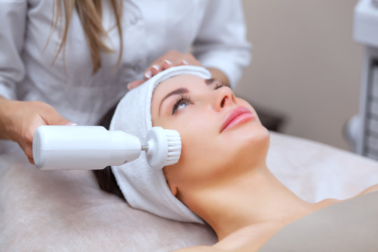 The cosmetologist makes the Hardware face cleaning  procedure with a soft rotating brush of a beautiful, young woman in a beauty salon. Cosmetology and professional skin care.