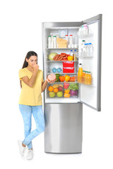 Young woman with expired sausage near open refrigerator on white background