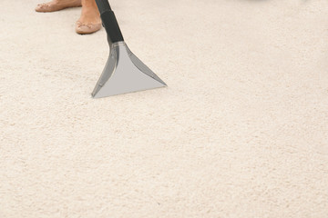 Woman removing dirt from carpet with vacuum cleaner indoors, closeup. Space for text