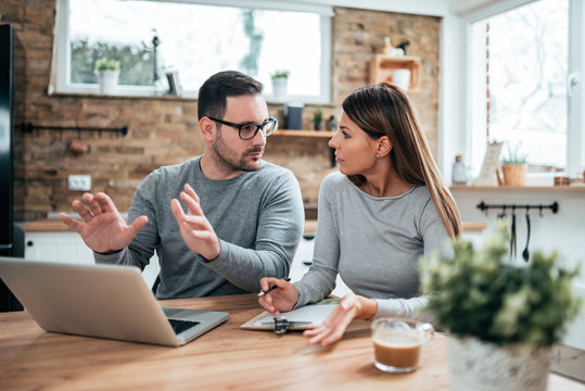 Young Couple Managing Their Family Budget, Sitting On The Kitchen.