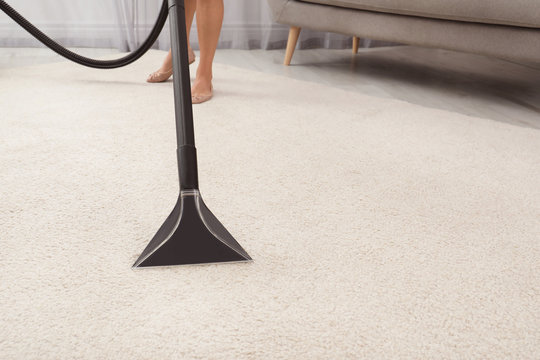 Woman removing dirt from carpet with vacuum cleaner indoors, closeup. Space for text