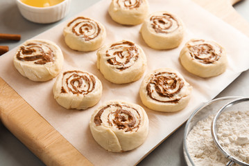 Wooden board with raw cinnamon rolls on table
