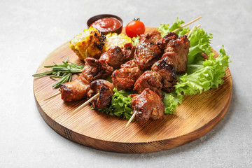 Wooden board with barbecued meat, garnish and sauce on grey background