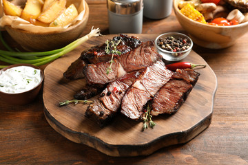 Serving board with delicious barbecued steak and spices on wooden table
