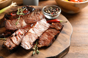 Serving board with delicious barbecued steak and spices on wooden table