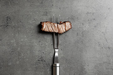 Fork with piece of delicious barbecued meat on gray background, top view