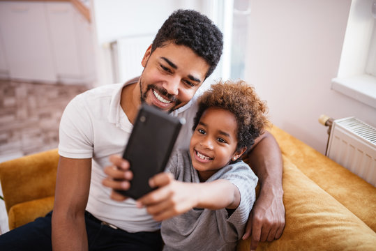 Mixed-race father and daughter taking a selfie at home.