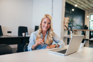 Beautiful blonde woman at workplace. Holding eyeglasses and looking at camera.