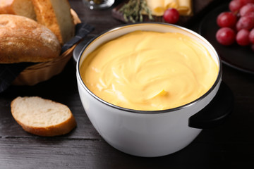 Pot with delicious cheese fondue on wooden table